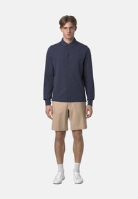Camicia a maniche lunghe color navy con bottoni e colletto, abbinata a pantaloni cargo beige, sneakers bianche e calzini bianchi a trama.