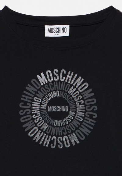 Μαύρο παιδικό μπλουζάκι με την επιγραφή «MOSCHINO» επαναλαμβανόμενη σε συγκεντρικούς κύκλους με ασημένια γκλίτερ στο μπροστινό μέρος και μια λευκή ετικέτα Moschino εσωτερικά στον γιακά.
