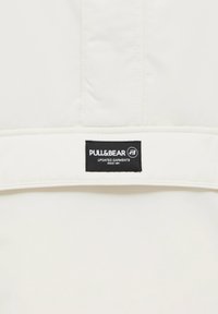 Vit tyg med en slät yta har en svart etikett som säger "PULL&BEAR UPDATED GARMENTS SINCE 1991" vid den nedre kanten.
