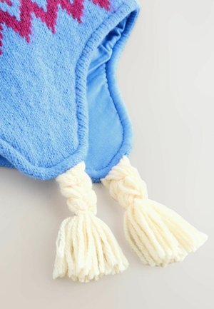 Sininen fleece-vaate, jossa on vaaleanpunainen sahalaitakuvio, ja jota koristavat punotut kerma-väriset tupsut alaosassa. Pehmeä rakenne ja pyöristetyt reunat.