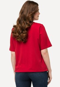Camiseta de algodón roja con mangas cortas, corte relajado, escote sencillo y textura suave, combinada con jeans de denim azul oscuro.