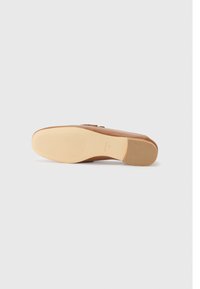 Chaussure plate en cuir tan avec une texture lisse et des détails subtils sur le dessus. Semelle extérieure en caoutchouc crème avec un motif rainuré pour une traction optimale.
