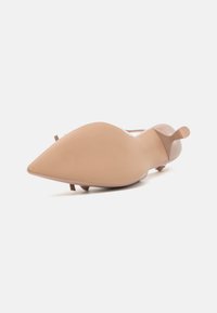 Νυφικά ψηλοτάκουνα παπούτσια σε γυμνό χρώμα με αιχμηρή μύτη, λεία επιφάνεια, μινιμαλιστικό σχέδιο και στενό ψηλό τακούνι που διαθέτει διακριτική ζώνη πίσω.