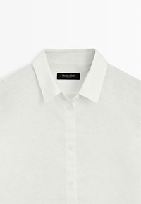 Camicia bianca in lino con bottoni, colletto appuntito e etichetta del marchio "Massimo Dutti" visibile all'interno del colletto.