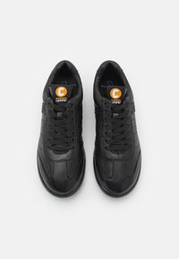 Mustad mustat nahast sneakersid ümarate varvastega, tasase tallaga ning tekstuursete paneelidega. Omavad musti nööre ja ümarat oranži logo keele peal.