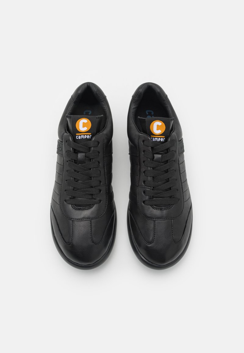 Black leather sneakers with a rounded toe, flat sole, and textured panels. Features black laces and a circular orange logo on the tongue.