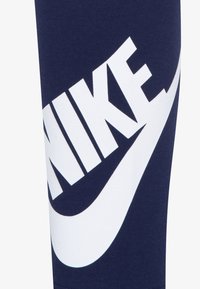 Mornarji modri bombažni legingi z velikim belim logotipom Nike in obliko paketa. Tkanina ima gladko teksturo in elastičen prileganje.