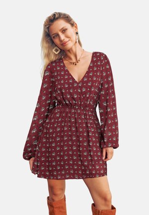 Robe bordeaux à manches longues et décolleté en V, ornée d'un motif floral. La taille est cintrée pour un effet froncé.