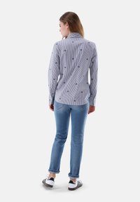 Striped shirt with small floral embroidery, long sleeves, button-down collar, paired with blue jeans and black and white sneakers.