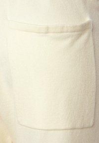 Hellbeige Stoff mit einer weichen, strukturierten Oberfläche zeigt eine rechteckige aufgesetzte Tasche auf einer flachen Fläche. Einfaches Design, keine zusätzlichen Akzente.