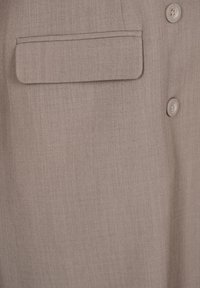 Camisa marrón claro con una textura suave, que presenta un bolsillo en el pecho y dos botones de tela, proporcionando un diseño limpio y a medida.