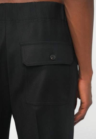 Calças pretas com um tecido texturizado, cintura elástica e um bolso lateral com fecho de botão na parte de trás.