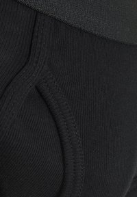 Sorte leggings med ribbet tekstur, elastisk talje og glat stof. Nærbillede af syningsdetaljer og tætsiddende design.