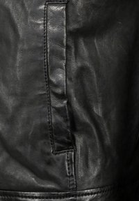 Textur eines schwarzen Lederjackets mit einer Seitentasche, die mit genähten Details und einer glatten Oberfläche versehen ist, und dabei die Weichheit und Haltbarkeit des Materials zur Schau stellt.