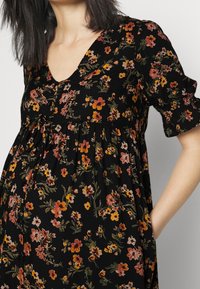 Schwarzes Blumenkleid mit kurzen Puffärmeln, einem V-Ausschnitt und einer gerafften Taille. Verziert mit orangefarbenen, pinken und grünen Blumen.
