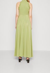Light green, floor-length dress with a halter neck, ruffled accents, and a shiny texture. Black block-heeled shoes visible below.