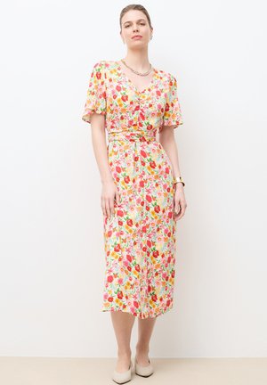 Frau trägt ein midi florales Kleid mit kurzen Ärmeln, V-Ausschnitt und geraffter Taille, steht vor einem schlichten weißen Hintergrund.