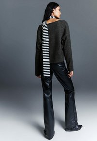 Pulover gri tricotat cu o eșarfă cu dungi alb-negru; asortat cu pantaloni din piele neagră lucioasă, evazați. Textură netedă, siluetă relaxată.
