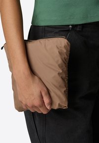 Brown padded clutch held in a hand, featuring a smooth outer material with a zip closure along the top. Worn with black pants.