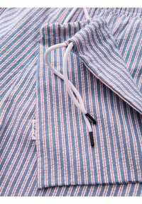 Tissu rayé bleu, blanc et rouge avec un cordon blanc passant par une section pliée et une petite étiquette en tissu attachée.