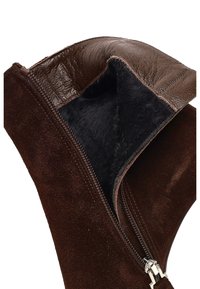 Interior de ante marrón con un forro negro suave, mostrando un borde de cuero marrón brillante y un detalle de cremallera plateada a lo largo de la abertura.