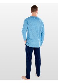 Maglietta azzurra a maniche lunghe con un motivo geometrico abbinata a pantaloni blu scuro. Materiale in cotone, vestibilità comoda e scollo rotondo.