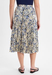 Knielanger, plissierter Rock in Creme mit blauem und schwarzem Blumenmuster. Elastischer Taillenbund, fließender Stoff und flache schwarze Sandalen.