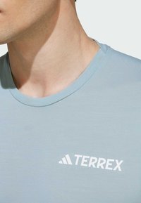 Világoskék, rövid ujjú póló, sima anyagból készült, fehér "TERREX" logóval a bal mellrészen, kerek nyakkivágással.