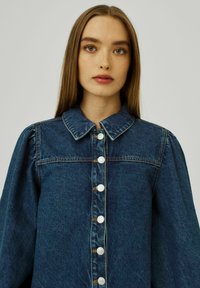 Denim jaka ar pieguļošu apkakli, pūkainām piedurknēm un sudraba pogām priekšpusē. Bagātīga zilā krāsa ar teksturētu apdari.