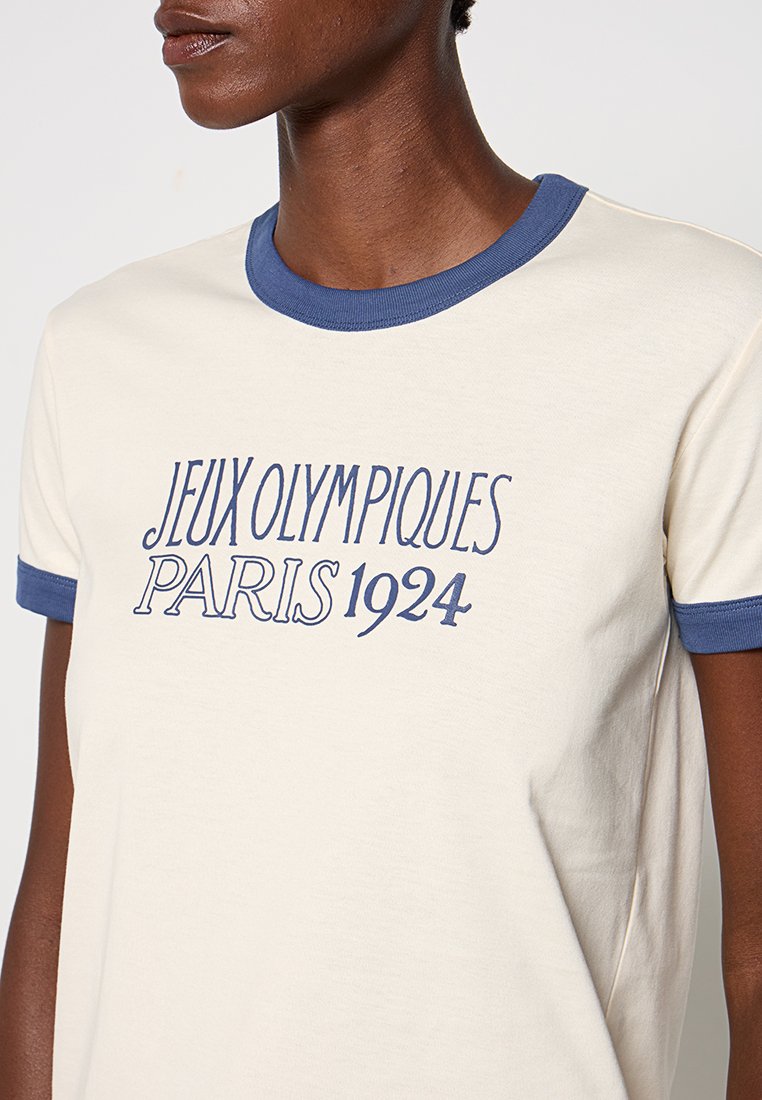 Cremefarbene Baumwoll-T-Shirt mit blauem geripptem Kragen und Ärmeln, mit dem Aufdruck "JEUX OLYMPIQUES PARIS 1924" auf der Vorderseite.