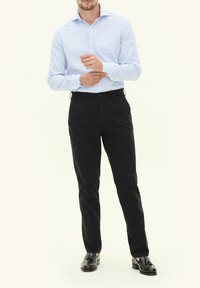 Camicia button-up a righe blu chiaro e bianche, abbinata a pantaloni neri e scarpe nere; presenta una tasca sul petto e una vestibilità sartoriale.