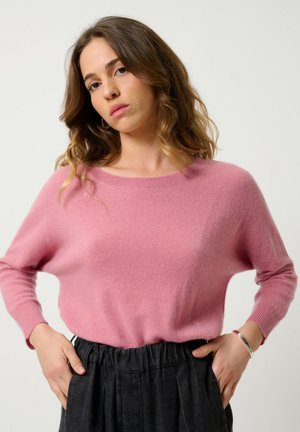 Pull en tricot rose avec une coupe décontractée et un col rond, associé à un pantalon sombre à taille élastique. Texture douce et design décontracté.