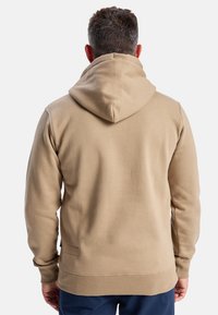 Tan hoodie met een relaxte pasvorm, geribde manchetten en zoom. Glad textuur, met een kangoeroezak en een klein label aan de zijkant.
