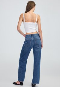 Niebieskie dżinsy w szerokim kroju z wysokim stanem i pięcioma kieszeniami, połączone z białym topem o krótkim kroju z teksturowanymi detalami dzianinowymi.