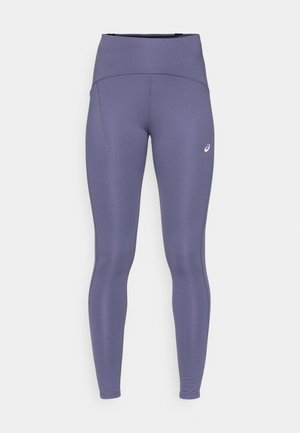 Leggings de tiro alto en color púrpura, fabricados con material elástico; cuentan con un bolsillo lateral y un pequeño logo en la parte baja de la pierna. Textura suave en toda la prenda.