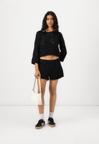 Zwarte crop top met geborduurd patroon, zwarte shorts, witte handtas met vetersluiting, zwarte sneakers en witte enkelsokken.