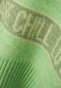 Green fleece fabric with a soft texture, featuring a prominent "CHILL OUT" graphic in a darker shade. Has ribbed edges for detail.