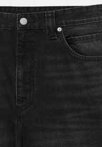 Gros plan sur un jean en denim noir montrant la taille, la passants de ceinture, le bouton, le rivet et les détails de la poche avant.