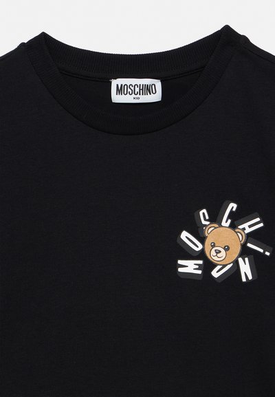Μαύρο παιδικό μπλουζάκι με στρογγυλή λαιμόκοψη, με σχέδιο πρόσωπο αρκουδάκι και διάσπαρτα λευκά γράμματα που σχηματίζουν τη λέξη "MOSCHINO" στο στήθος.