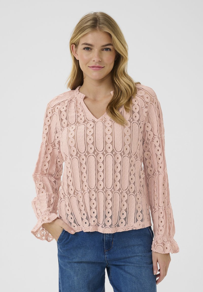 Svetlo roza čipkast zgornji del s V-izrezom, dolgimi rokavi z nabranimi manšetami in zapletenimi izseki. Ujemite ga z modrim jeansom.