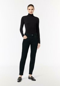 Zwarte coltrui gecombineerd met donkergroene, slim fit jeans, met een voorste knoopsluiting, zakken en een gladde textuur.