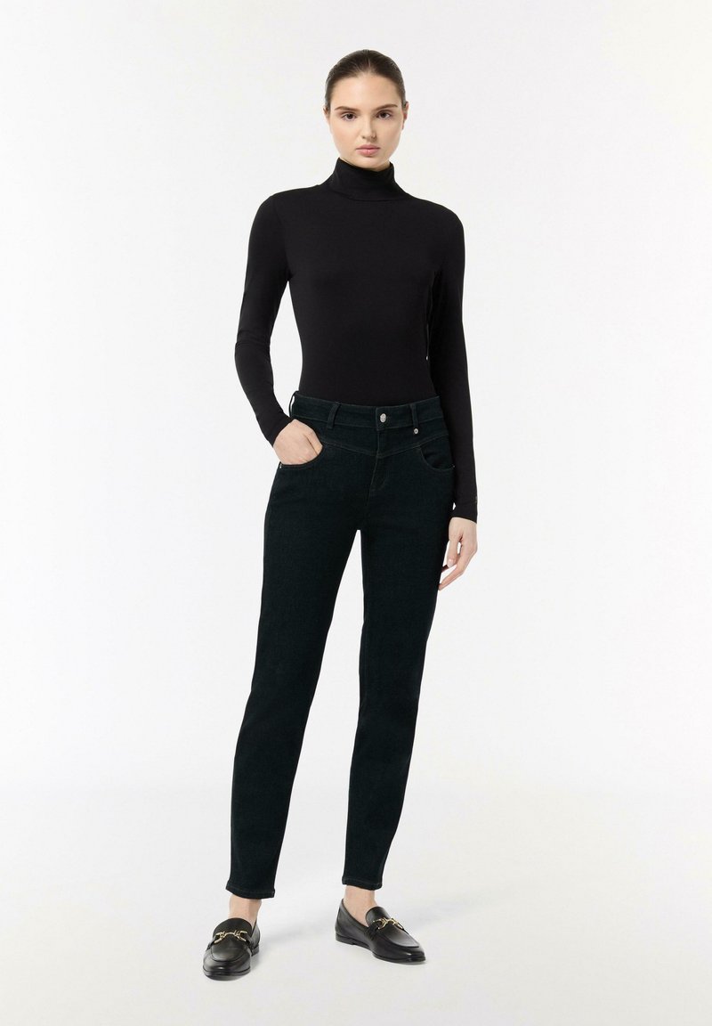 Zwarte coltrui gecombineerd met donkergroene, slim fit jeans, met een voorste knoopsluiting, zakken en een gladde textuur.