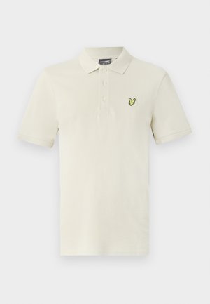 Világos bézs színű, pamut póló, három gombos gallérral és egy kis zöld madár emblémával a bal mellrészen. Rövid ujjak.