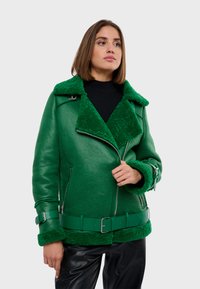 Zelená kožená bunda so štruktúrovaným zeleným fleecovým golierom a manžetami, so zipsom na prednej strane, bočnými vreckami a zodpovedajúcim opaskom.