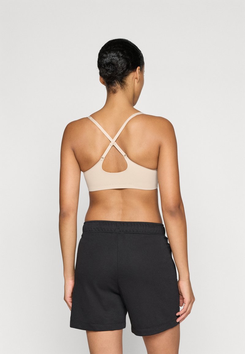 Reggiseno sportivo nudo con spalline incrociate e dettaglio a chiave, abbinato a pantaloni corti neri con vita elastica. Texture liscia, design aderente.