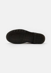 Suela de zapatilla negra de material de goma, con un patrón texturizado para el agarre y detalles del logo cerca del arco.