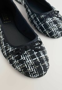 Schwarz-weiße gemusterte Ballettschuhe mit einem strukturierten Obermaterial, das eine schwarze Akzent-Schleife und ein rundes Zehendesign aufweist.