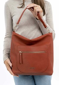 Sac à main en cuir rouge texturé au design souple, avec une poche avant zippée et une bandoulière robuste. Accents en matériel doré.
