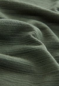 Teksturowana zielona tkanina z delikatnym połyskiem, prezentująca subtelnym prążkowanym wzorem i miękką, zwisającą jakością. Doskonała do użycia w odzieży lub tapicerce.