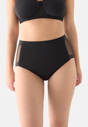 Mujer con ropa interior negra de talle alto con paneles laterales transparentes, combinada con un sujetador negro, mostrada desde el torso hasta la mitad del muslo.
